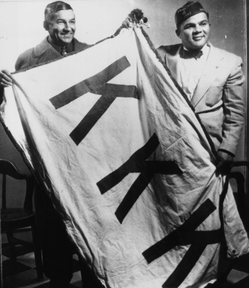 Two Lumbee men, Charlie Warriax (left) and Simeon Oxendine (right), displaying the KKK flag they stole from the Klan following their victory in the Battle of Hayes Pond.